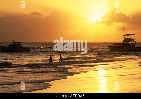 Zwei Menschen waten durch die Wellen, wenn die Sonne in Barbados untergeht Stockfoto