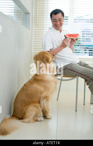 Reifer Mann hält ein Stück Wassermelone Blick auf seinen Hund Stockfoto