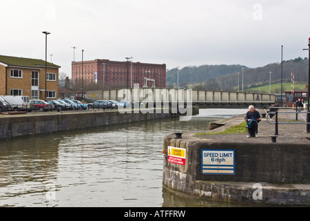 Ein Mann liest, während er wartet für das Wassertaxi in Bristol Hafen A Tabaklager ist im Hintergrund wie eine Drehbrücke Stockfoto