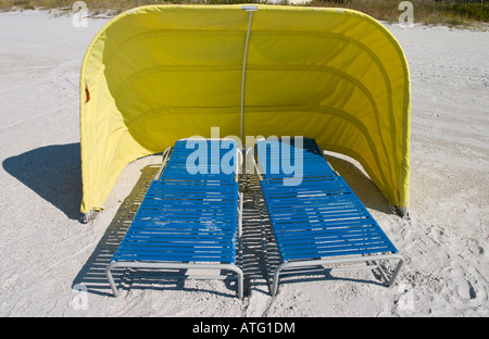 Windschutz in gelb. Zwei blaue Strand liegen unter einer gelben Leinwand Wind und Sonne Schatten an einem weißen Sandstrand Stockfoto