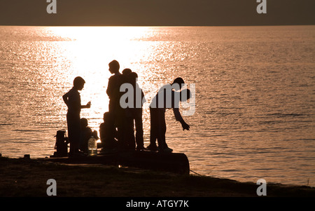 Angeln vom Dock aus einer Gruppe von jungen in Silhouette Chats und Fisch aus einem kleinen Hafenbecken an der Seite des Sees Stockfoto