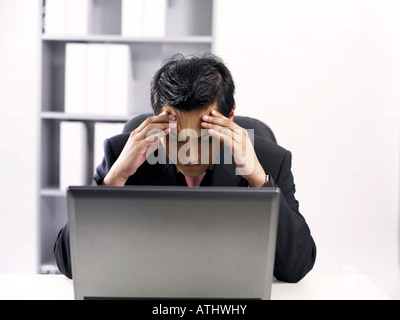 Geschäftsmann mit Kopfschmerzen mit Blick auf sein Werk Stockfoto