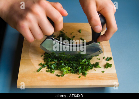 Hacken von Blattpetersilie Mezzaluna mit Holzbrett Stockfoto