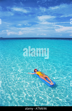 Frau im Paradies auf Luftmatratze zwischen klaren Aqua blauen Wasser und weißen Wolkenfetzen entspannend Stockfoto