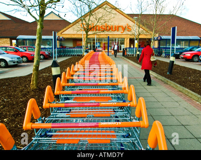 Frau Shopper unterwegs zu Sainsburys Supermarkt neben einer Reihe von trolleys Stockfoto