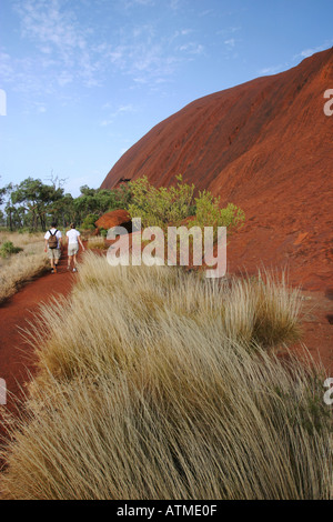 Touristen auf der kreisförmigen Wanderweg rund um Ayers Rock verschwindet in der Ferne im morgendlichen Sonnenlicht Australien Stockfoto