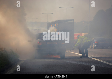 NOTDIENSTE MIT FEUERLÖSCHER AUF BRENNENDE AUTO AUF M62 AUTOBAHN HARTE SCHULTER Stockfoto