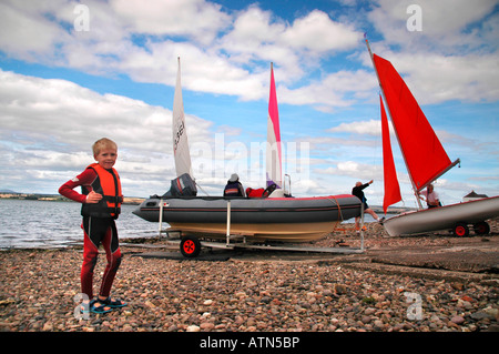 Ein kleiner Junge posiert mit Jollen im Hintergrund während des Wartens auf Segeln gehen Stockfoto