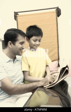 Mitte erwachsener Mann liest eine Zeitung mit seinem Sohn und lächelnd Stockfoto