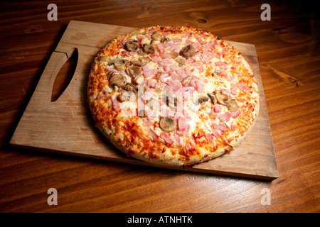 Eine große Pizza mit Käse, Schinken und Pilzen. Pizza wird auf einem Holzbrett gekocht und wirkt sehr appetitlich und lecker. Stockfoto