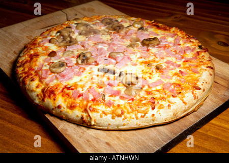 Eine große Pizza mit Käse, Schinken und Pilzen. Pizza wird auf einem Holzbrett gekocht und wirkt sehr appetitlich und lecker. Stockfoto