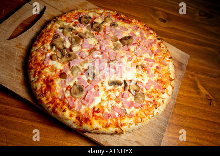 Eine große Pizza mit Käse, Schinken und Pilzen. Pizza wird auf einem Holzbrett gekocht und wirkt sehr appetitlich und lecker. Stockfoto