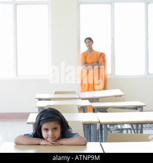 Porträt einer Schülerin stützte sich auf einen Schreibtisch mit einem Lehrer im Hintergrund stehend Stockfoto