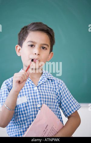 Porträt von Schuljunge hält einen Stift und ein Buch vor einer Tafel Stockfoto