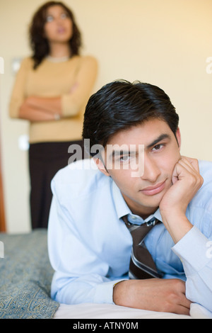 Porträt eines Geschäftsmannes, liegend auf dem Bett mit einer jungen Frau im Hintergrund stehend Stockfoto