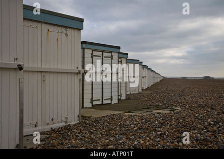 Blick nach Osten entlang einer Linie von Strandhütten mit Worthing Pier im Hintergrund. Worthing, West Sussex, England. Stockfoto