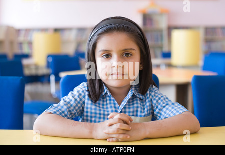 Porträt einer Schülerin mit ihren Händen umklammert sitzen in einer Bibliothek Stockfoto