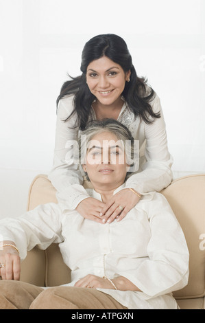 Porträt einer reifen Frau sitzen auf einer Couch und ihre Tochter, umarmen sie von hinten Stockfoto
