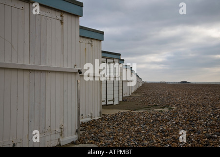 Blick nach Osten entlang einer Linie von Strandhütten mit Worthing Pier im Hintergrund. Worthing, West Sussex, England. Stockfoto