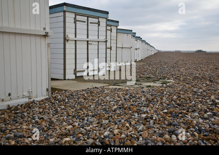 Blick nach Osten entlang einer Linie von Strandhütten mit Worthing Pier im Hintergrund. Worthing, West Sussex, England. Stockfoto