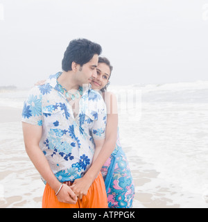 Junge Frau umarmt einen jungen Mann von hinten am Strand Stockfoto