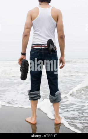 Rückansicht eines jungen Mannes Stand am Strand mit der holding ein flip-flop Stockfoto