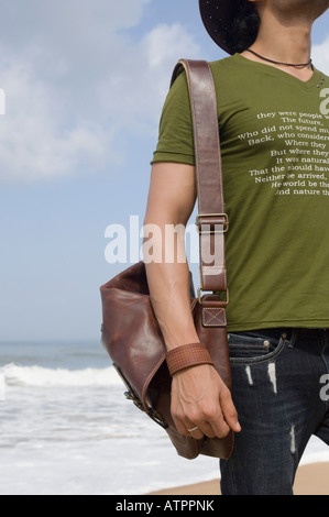Junger Mann stehen am Strand und eine Tragetasche Stockfoto