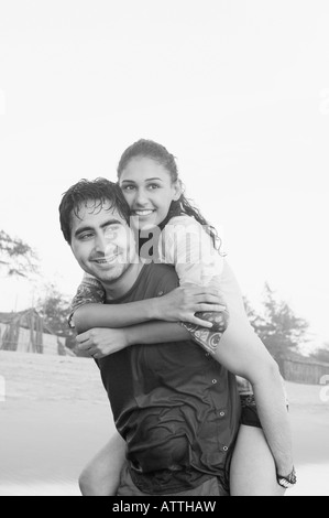 Junger Mann lächelnd und eine junge Frau auf dem Rücken Huckepack Stockfoto