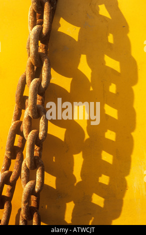 Detail der heavy-Duty Metallkette leicht verrostet und Casting interessante Schatten auf gelb lackierten Oberfläche Stockfoto