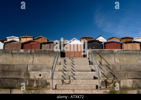 Frinton am Meer Strandhütten hinter der gekrümmten Beton Ufermauer vor blauem Himmel Stockfoto