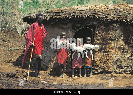 Maasai Jugend und drei Mädchen hält Baby Ziegen außerhalb traditioneller Lehm und Flechtwerk Hütte in der Nähe von Masai Mara National Reserve Kenya Stockfoto