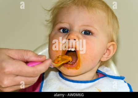 Horizontale Nahaufnahme von einem hübschen kaukasischen Babymädchen in einen Hochstuhl zum Abendessen mit Lebensmitteln über das ganze Gesicht Stockfoto