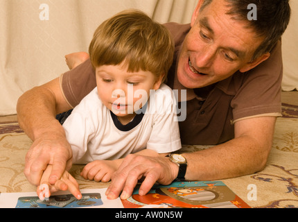 Großvater-Vater-Lesung am Boden mit Enkel Sohn zwei Jahre alt Stockfoto