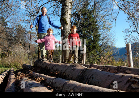 Kinder, die bei ihrem Großvater auf hölzernen Baumstämmen balancieren Stockfoto