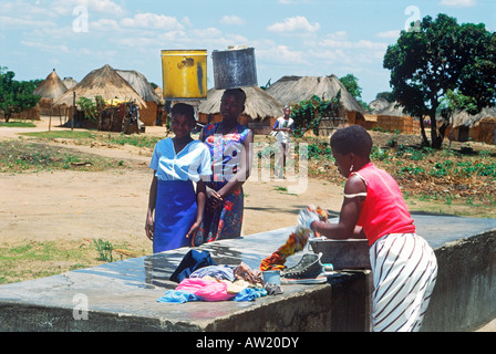 Junge Mädchen, die Portierung schwere Eimer Wasser vorbei an Frau Waschen von Kleidung in Simbabwe Dorf Stockfoto