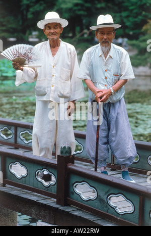 Zwei ältere Männer in leichten Leinen-Outfits mit Hüten und Hand statt Ventilatoren für heiße Sommertage in Südkorea Stockfoto