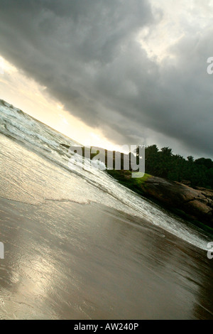Dunkle Wolken über einem Strand kurz vor Sonnenuntergang in Kerala eine stimmungsvolle Atmosphäre vermittelt Stockfoto