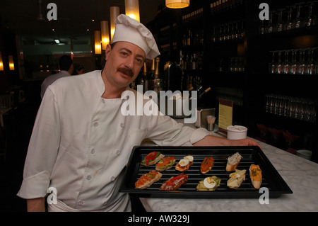 Ein Koch präsentiert ein Tablett mit Tapas Vorspeisen oder Snacks, serviert auf kleinen Brotscheiben, die oft als Montaditos oder Pintxos Spanien bezeichnet werden Stockfoto