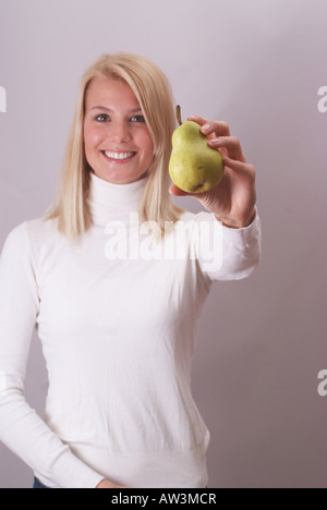 Blonde Frau hält eine Birne Lächeln | Laechelnde Junge Blonde Frau Haelt Eine Birne Stockfoto