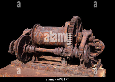 Eine alte, rostfreie Eisenwinde mit Trommel, Zahnrädern und Schwungrädern, auf einem Holzsockel vor schwarzem Hintergrund montiert - Industriearchitekologie, Funchal, Madeira, Portugal. Stockfoto