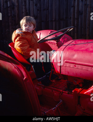 kleiner Junge sitzt auf alten roten Traktor Stockfoto