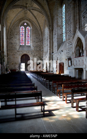 Innenansicht des Abbaye de Lehon Brittany mit einem Buntglasfenster, Kirchenbänken, der Kanzel und einem durch ein anderes Fenster strahlenden Licht Stockfoto