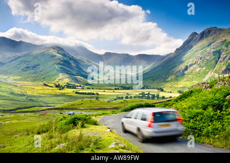 Autos in Bewegung auf einer Landstraße über Great Langdale Valley mit Blick in Richtung der Band, Bowfell und Langdale Pikes. Lake District, Großbritannien Stockfoto