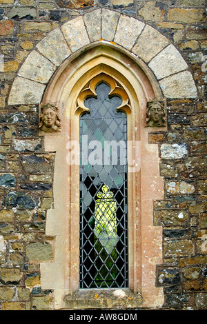 Architektonisches Detail nahe, von einem gotischen gewölbt Kirchenfenster mit steinernen Gesichtern jeder Seite und klar verbleites Glas Stockfoto