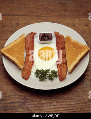Frühstück Teller Platte ein Spiegelei Sonnenseite, zwei Scheiben Toast Traubengelee Petersilie Speckplatte auf hölzernen Tischplatte Stockfoto