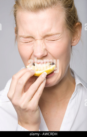 Junge Frau in eine Zitrone beißt und machen ein lustiges Gesicht Stockfoto