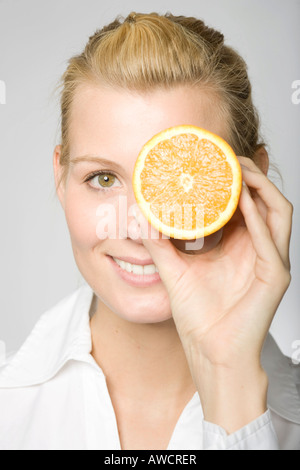 Blonde Frau lachend mit in Scheiben geschnittenen Orange vor einem Auge Stockfoto