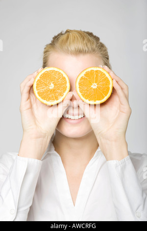 Blonde Frau lachend mit zwei in Scheiben geschnittene Orangen vor ihren Augen Stockfoto