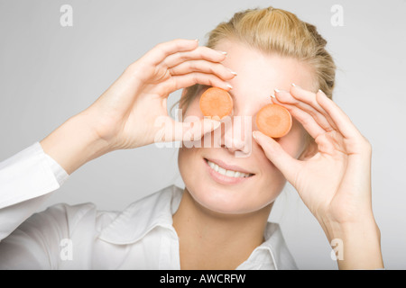 Junge blonde Frau mit zwei Karotten Scheiben vor ihren Augen Stockfoto