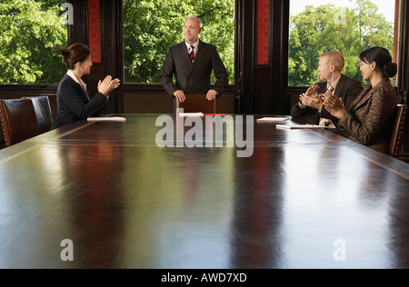 Geschäftsleute um Konferenztisch, applaudieren Mann Stockfoto